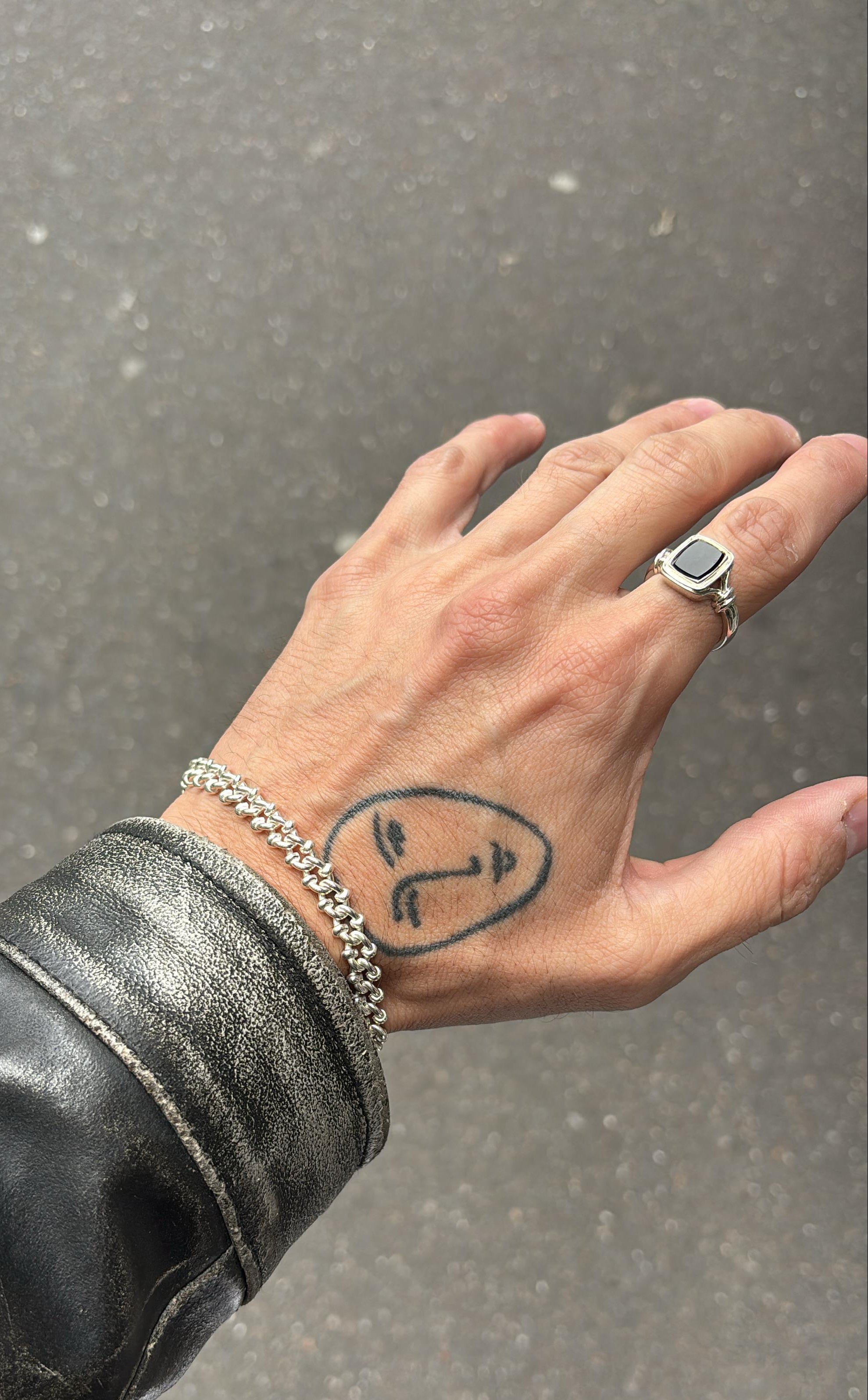 Hand with tattoo and jewelry on a gray pavement background